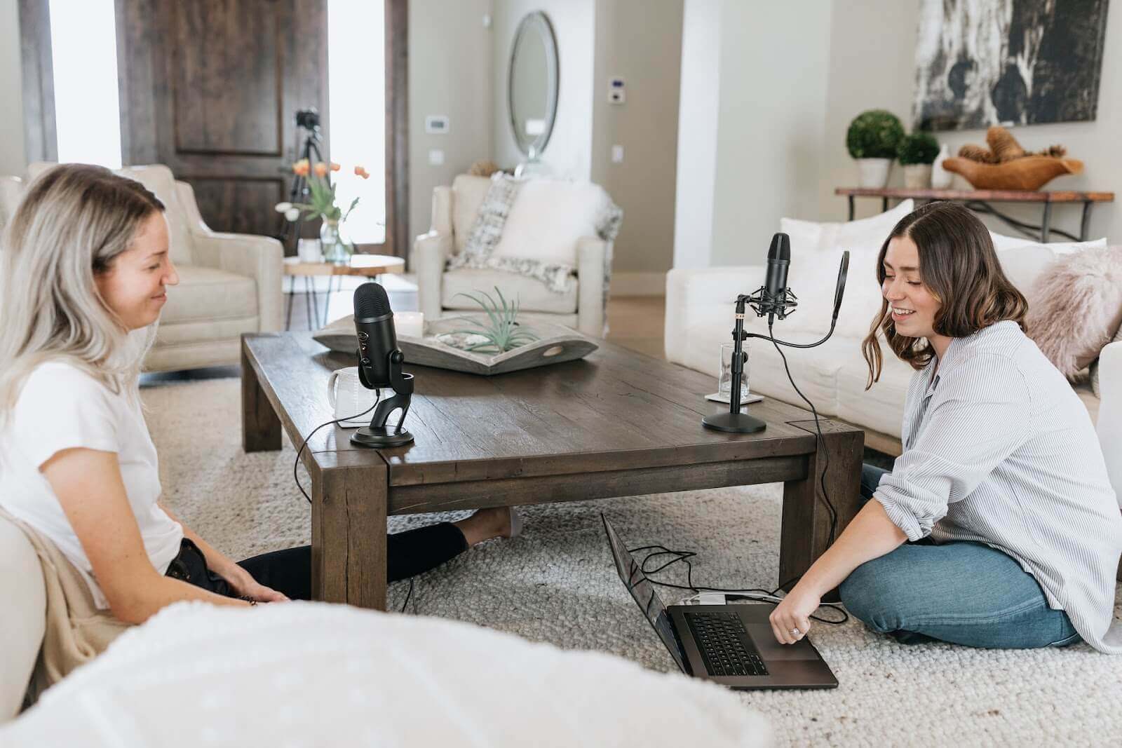 Two women chatting during podcast in living room, surrounded by pillows and carpet